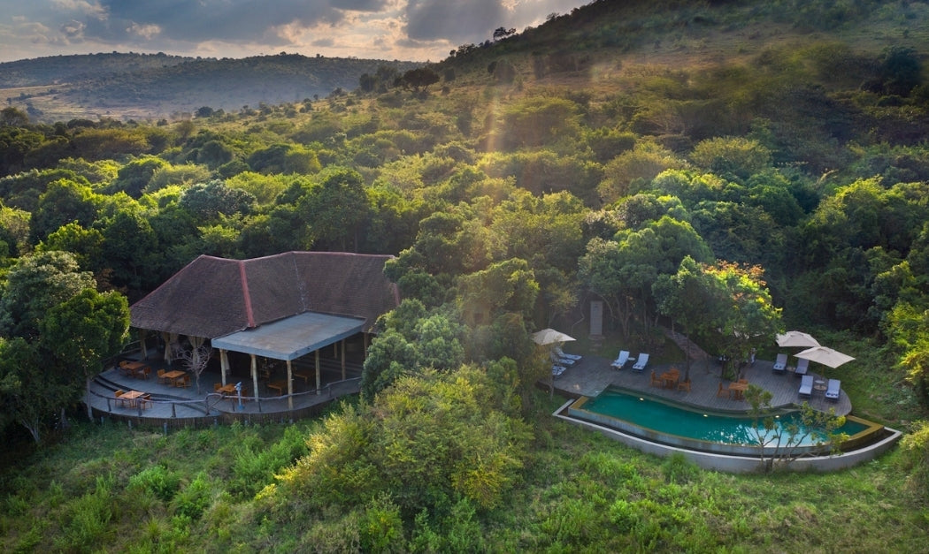 Aerial view of luxury safari lodge nestled in lush greenery in the Masai Mara with pool and thatched-roof suites